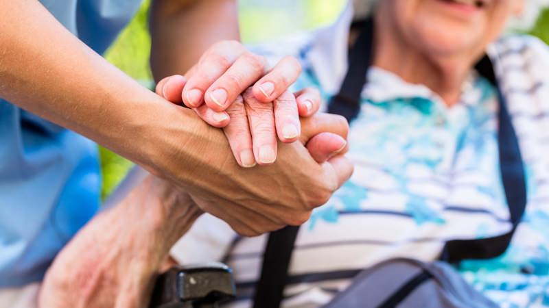 Vårdpersonal håller äldre människa i handen